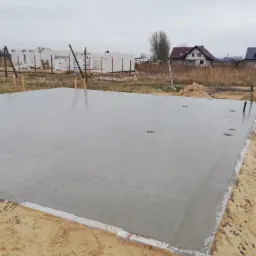 Wylany, świeży fundament pod budowę domu w Dłużynie, widoczne wystające pręty zbrojeniowe i początek wznoszenia ścian z bloczków betonowych w tle.