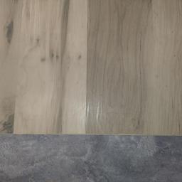 Świat Komfortu - Detale połączenia jasnych paneli podłogowych imitujących drewno z szarą, kamienną posadzką.