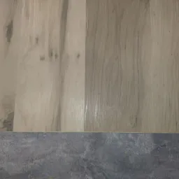Detale połączenia jasnych paneli podłogowych imitujących drewno z szarą, kamienną posadzką.