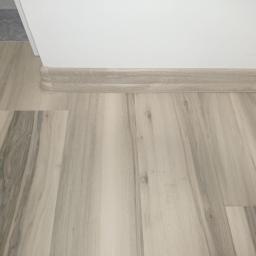 Świat Komfortu - Jasne panele podłogowe z wzorem drewna, listwa przypodłogowa w kolorze paneli, widok z niskiej perspektywy.