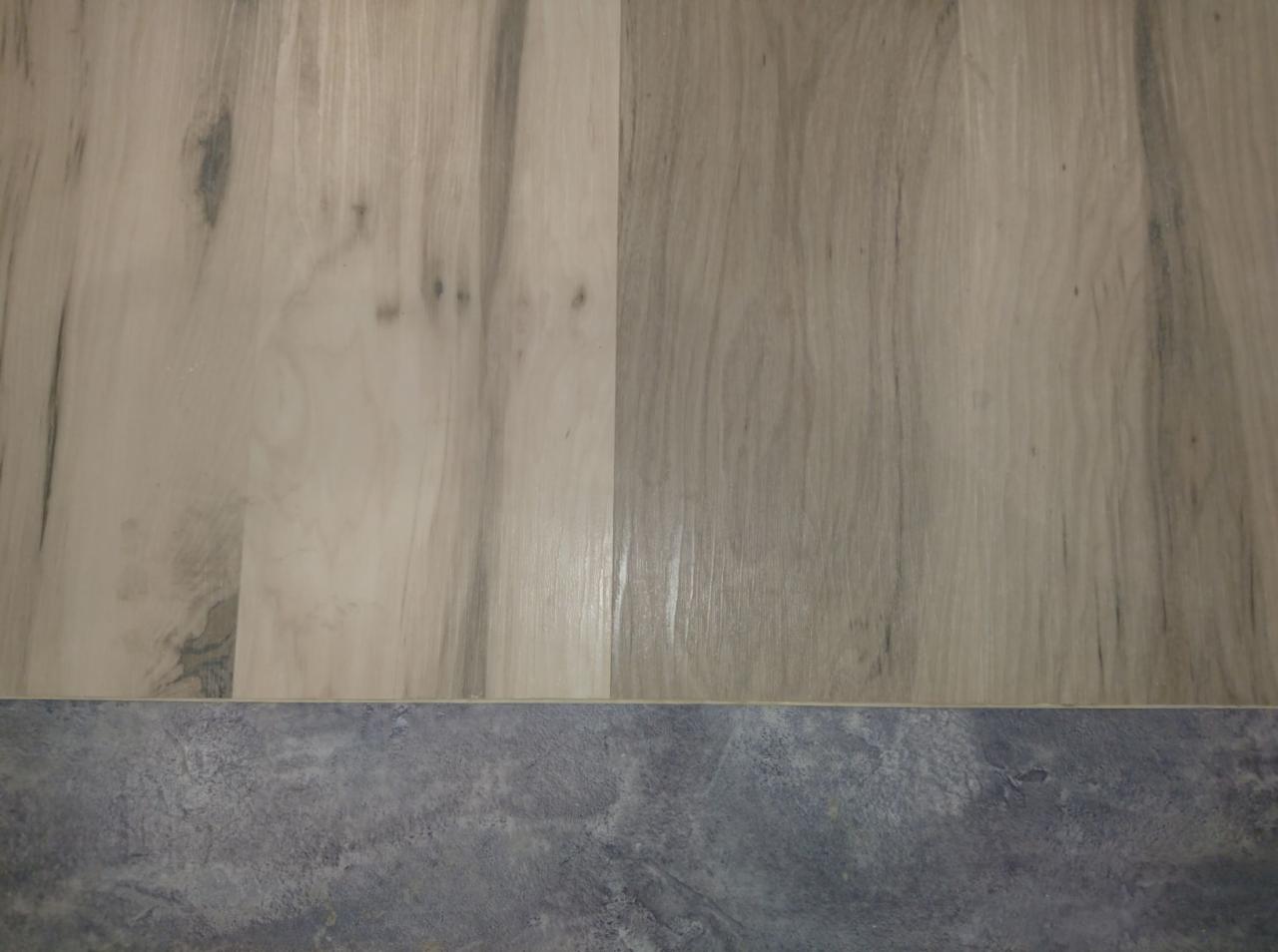 Detale połączenia jasnych paneli podłogowych imitujących drewno z szarą, kamienną posadzką.