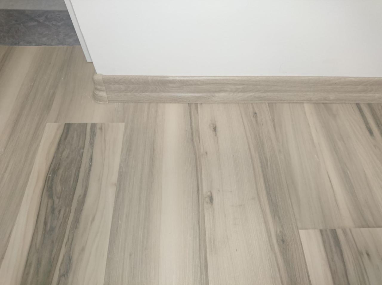 Jasne panele podłogowe z wzorem drewna, listwa przypodłogowa w kolorze paneli, widok z niskiej perspektywy.