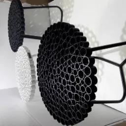 Trzy okrągłe panele dekoracyjne z rurek PCV w kolorze białym i czarnym, zamocowane na metalowych stelażach, tworzące geometryczny wzór na białej ścianie.