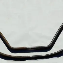 Dwie gięte, metalowe konstrukcje z zakręconymi zakończeniami, prawdopodobnie fragmenty balustrady, leżące na jasnym tle.