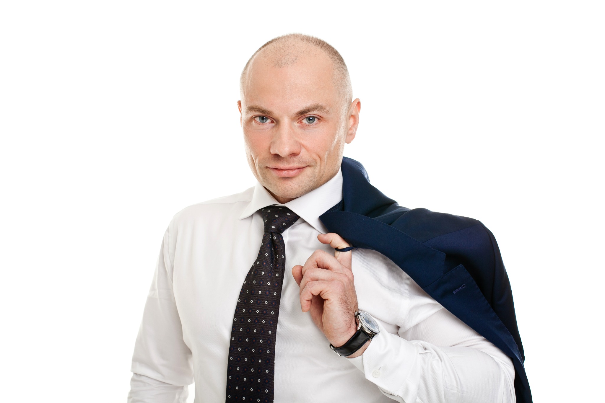 Mężczyzna w białej koszuli i krawacie, z marynarką na ramieniu, patrzy w obiektyw. Widoczny zegarek na nadgarstku. Białe tło.