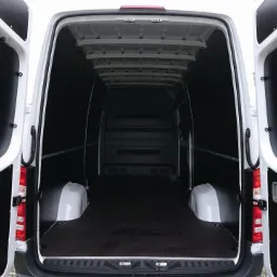 Wnętrze białego furgonu z otwartymi tylnymi drzwiami, wyłożone czarną płytą, gotowe do załadunku.