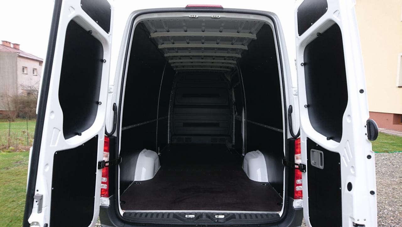 Wnętrze białego furgonu z otwartymi tylnymi drzwiami, wyłożone czarną płytą, gotowe do załadunku.