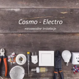 Aranżacja narzędzi i akcesoriów elektrycznych, w tym przewody, szczypce, włącznik, gniazdko, żarówki LED, złączki i taśma izolacyjna, ułożonych na rustykalnym drewnianym tle z logo 'Cosmo-Electro'...