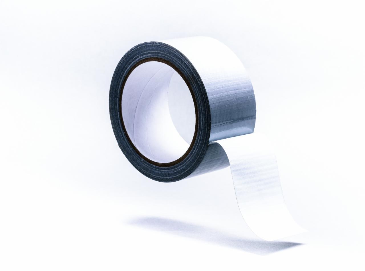 Rolka srebrnej taśmy naprawczej na białym tle, z odwijającym się fragmentem, ukazująca fakturę materiału.