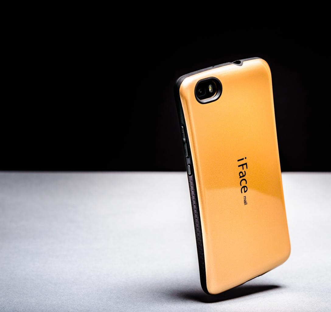 Złoty futerał iFace na smartfon, ustawiony pionowo na szarym tle z czarnym tłem, widoczne boczne przyciski i otwór na aparat.