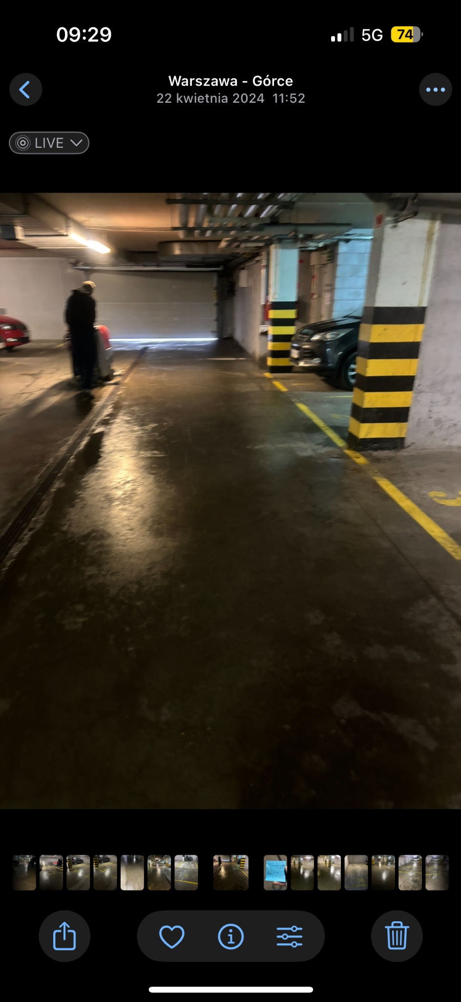 Czyszczenie posadzki w garażu podziemnym. Osoba obsługuje maszynę czyszczącą, widoczne mokre ślady po umyciu. Słabe oświetlenie, żółte pasy na podłodze.