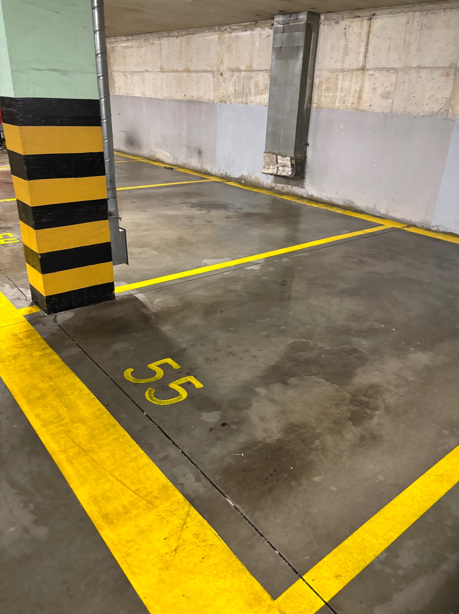 Oczyszczona posadzka parkingu podziemnego w Warszawie, z żółtymi liniami i numerem 55, po sprzątaniu. Widoczny słup z pasami ostrzegawczymi i betonowe ściany.