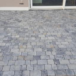 Vitto - Ułożona szara kostka brukowa na podjeździe przed domem, widoczne przesuwne drzwi tarasowe i fragment elewacji.