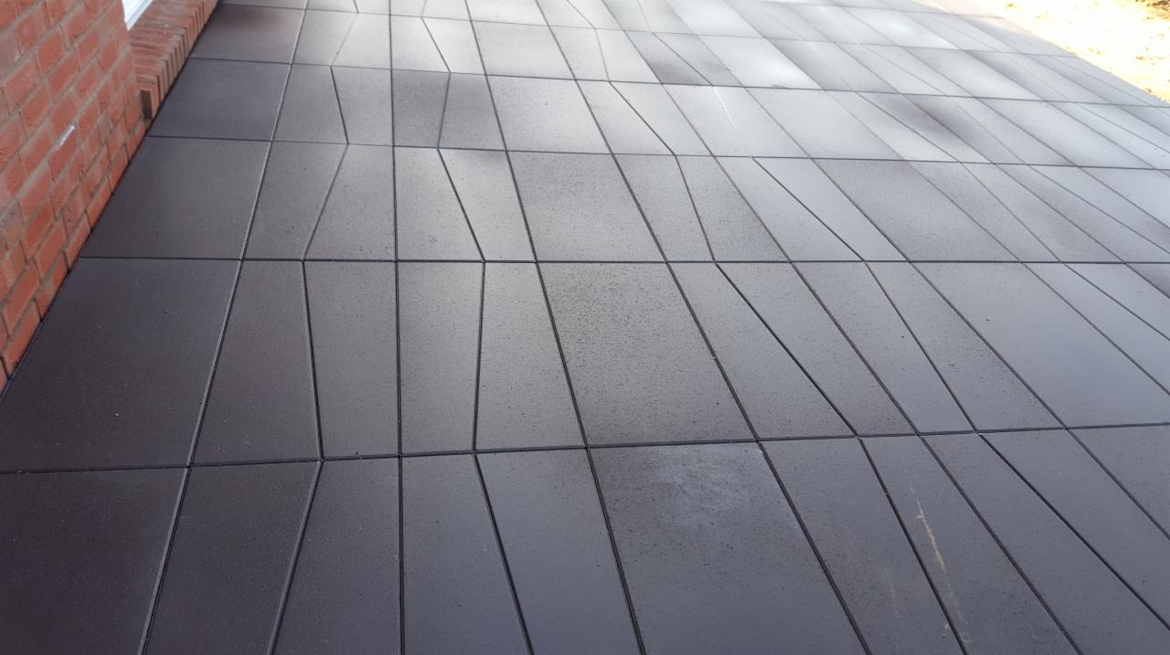 Nisko kątowe ujęcie ciemnoszarej nawierzchni z kostki o nieregularnym kształcie, przylegającej do ceglanej ściany budynku.