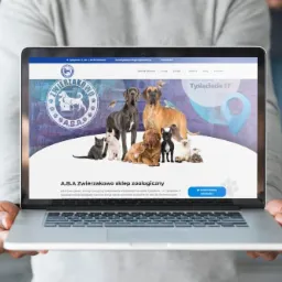 Osoba trzyma laptopa prezentującego stronę internetową sklepu zoologicznego 'A.B.A Zwierzakowo' z grafiką psów i kotów na tle mapy Katowic.