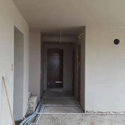 Wnętrze w Dziembowie w trakcie prac przygotowawczych do wykończenia: ściany po szpachlowaniu, widoczne kable i instalacje podłogowe, surowy stan przed malowaniem.