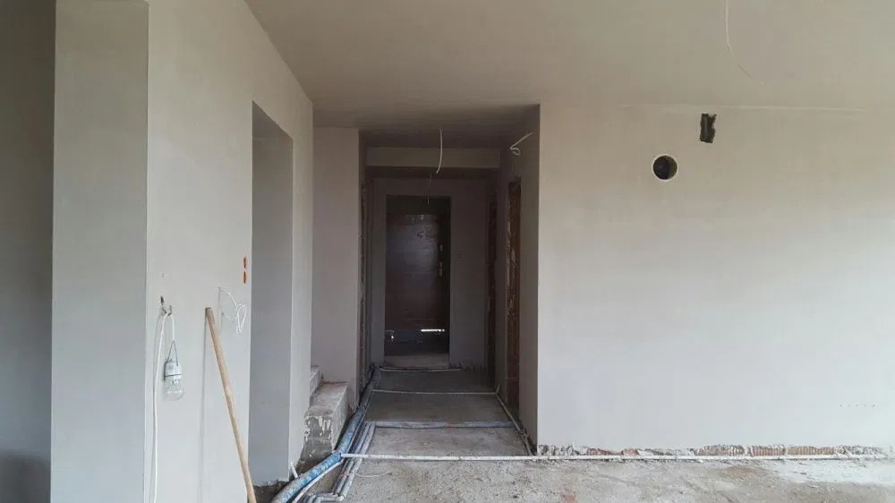 Wnętrze w Dziembowie w trakcie prac przygotowawczych do wykończenia: ściany po szpachlowaniu, widoczne kable i instalacje podłogowe, surowy stan przed malowaniem.
