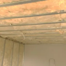 Montaż sufitu podwieszanego z widoczną izolacją wełnianą, metalowy stelaż z profilami CD i UD, instalacja elektryczna w trakcie prowadzenia.