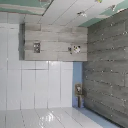 Świeżo ułożone, białe i szare płytki imitujące drewno na ścianach i podłodze łazienki w trakcie prac wykończeniowych, z widocznymi krzyżykami dystansowymi i otworami na instalacje.