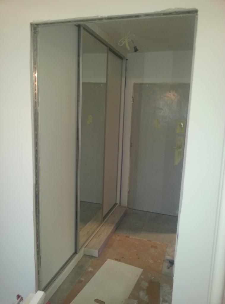 Montaż szafy wnękowej z przesuwnymi drzwiami, widoczne profile i nieukończona podłoga w tle.