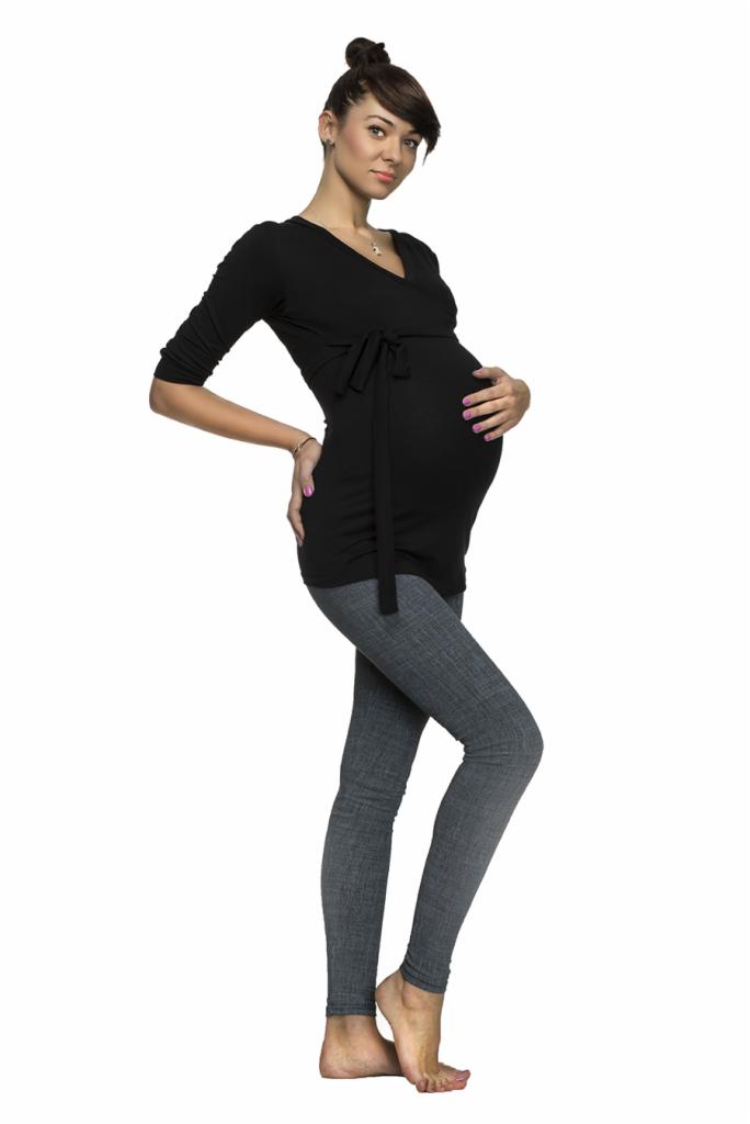 Kobieta w ciąży pozuje w czarnej bluzce z wiązaniem i szarych legginsach na białym tle.