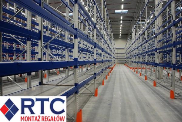 Wnętrze hali magazynowej z zamontowanymi, wysokimi regałami paletowymi w kolorze srebrnym i niebieskim, z pomarańczowymi osłonami słupów, widok w perspektywie zbieżnej.