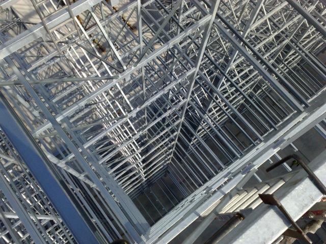 Szkielet dachu hali z profili stalowych, widok z góry na konstrukcję kratownicową, elementy złączone spawami i śrubami, szare profile, surowy stan wykończenia.