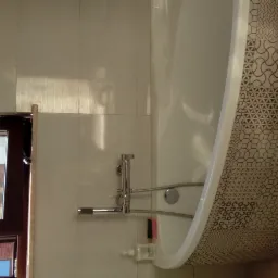 Biała wanna obudowana płytkami z geometrycznym wzorem, bateria wannowa z mydłem w płynie obok, okno w ciemnej ramie.