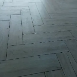 Szare panele ułożone we wzór jodełki francuskiej, widoczne delikatne usłojenie drewna, matowe wykończenie, perspektywa z dołu.