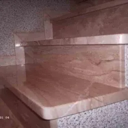 Wykończone marmurowe schody wewnętrzne z widoczną fakturą kamienia i połączeniem z szarą ścianą o drobnej strukturze.