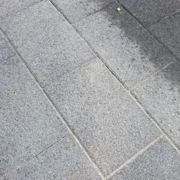 Ułożona kostka brukowa w szarym odcieniu, widoczny fragment chodnika z obrzeżem.