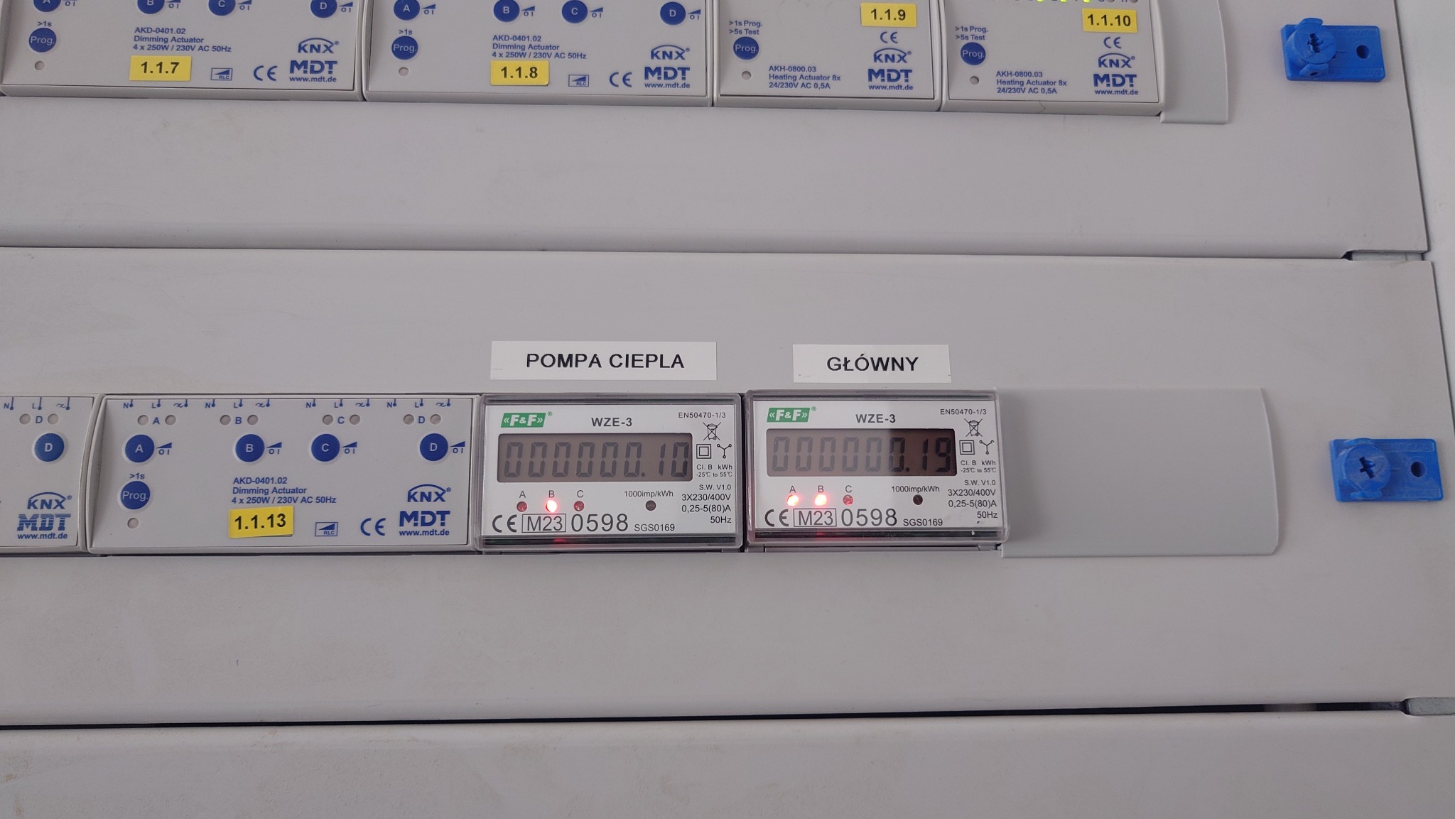 Szare panele elektryczne z modułami KNX i licznikami energii elektrycznej F&F WZE-3 oznaczonymi jako 'Pompa Ciepła' i 'Główny', widoczne wartości zużycia energii.