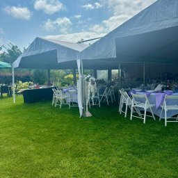 SMAKPOL-CATERING sp. z o.o. - Biały namiot plenerowy na trawie, przygotowany na uroczystość. Stoły z fioletowymi obrusami i białymi krzesłami, dekoracje kwiatowe. Słoneczny dzień.