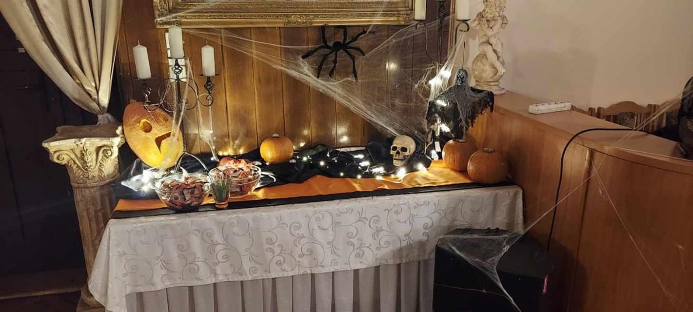 Dekoracja stołu na Halloween: dynie, czaszka, pająk, świece, pajęczyna, duch. Aranżacja w ciemnych barwach z pomarańczowymi akcentami.