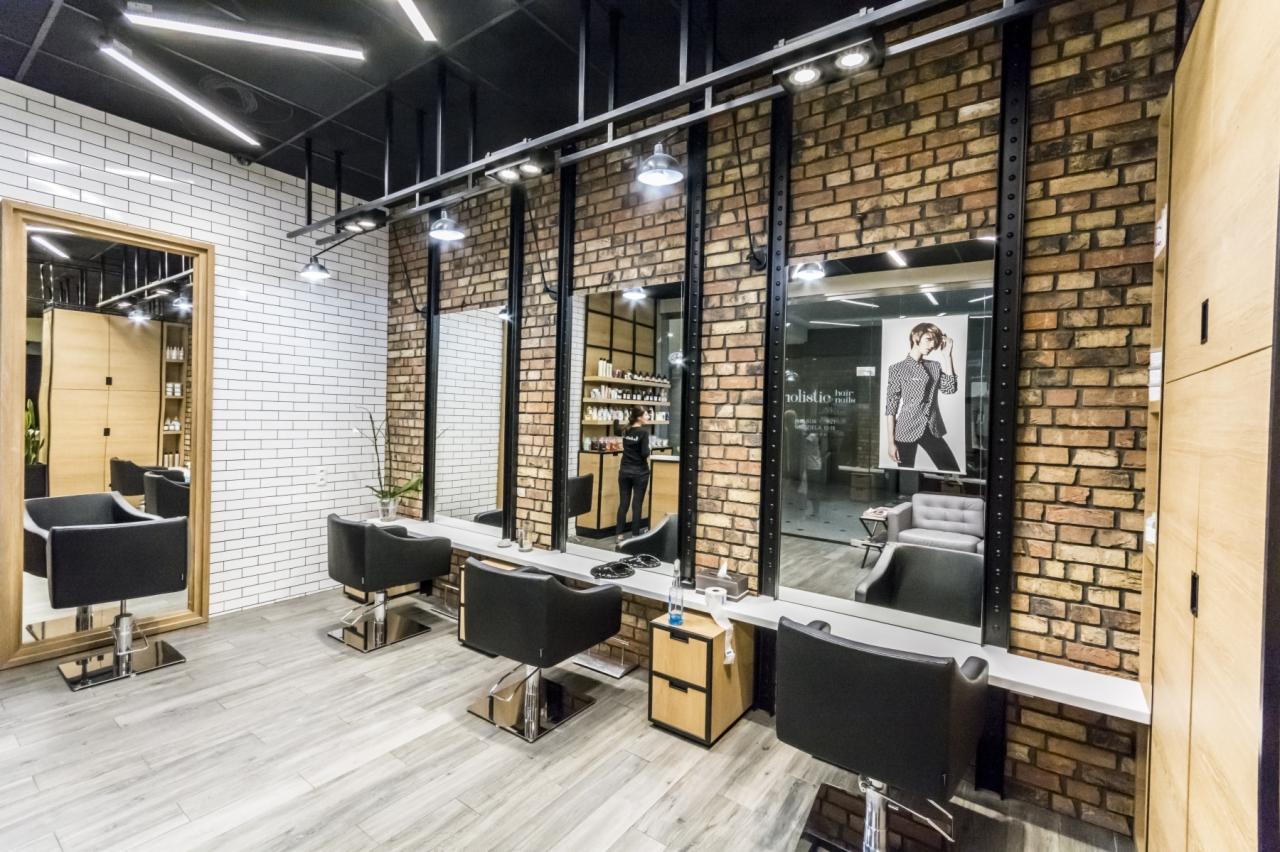 Nowoczesne wnętrze salonu z ceglaną ścianą, trzema stanowiskami fryzjerskimi z dużymi lustrami, czarnymi fotelami i drewnianą podłogą imitującą deski.