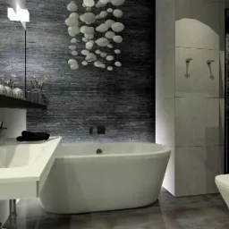 Nowoczesna łazienka z kamienną ścianą, białą wanną wolnostojącą, umywalką nablatową i dekoracyjną lampą sufitową z białych kul.