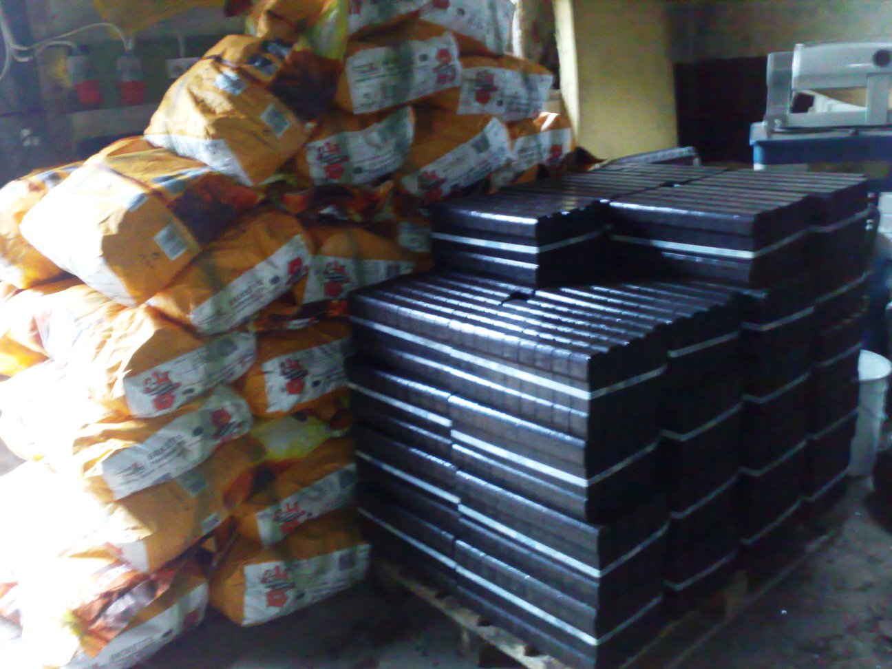 Stos pakowanych worków z brykietem i ułożone kostki brykietu na palecie w magazynie.