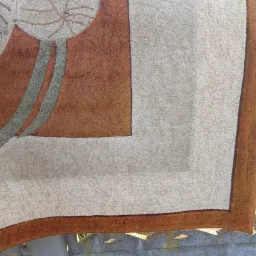 Wysuszony dywan z geometrycznym wzorem liścia i brązowymi akcentami, suszący się na szorstkim betonowym murku.