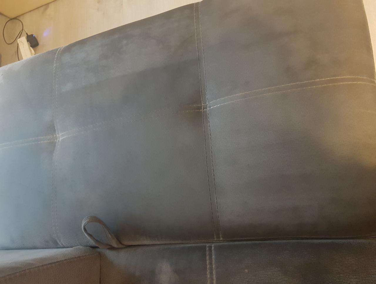 Szara kanapa z widocznym efektem czyszczenia - jaśniejszy pas po lewej stronie, ciemniejszy po prawej, z uchwytem z boku.