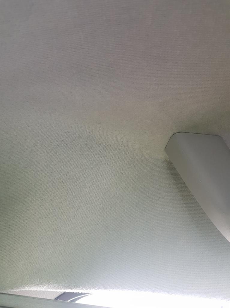 Jasnoszara podsufitka samochodu z widocznym uchwytem, ukazująca delikatną fakturę materiału.