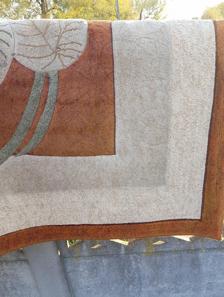 Wysuszony dywan z geometrycznym wzorem liścia i brązowymi akcentami, suszący się na szorstkim betonowym murku.