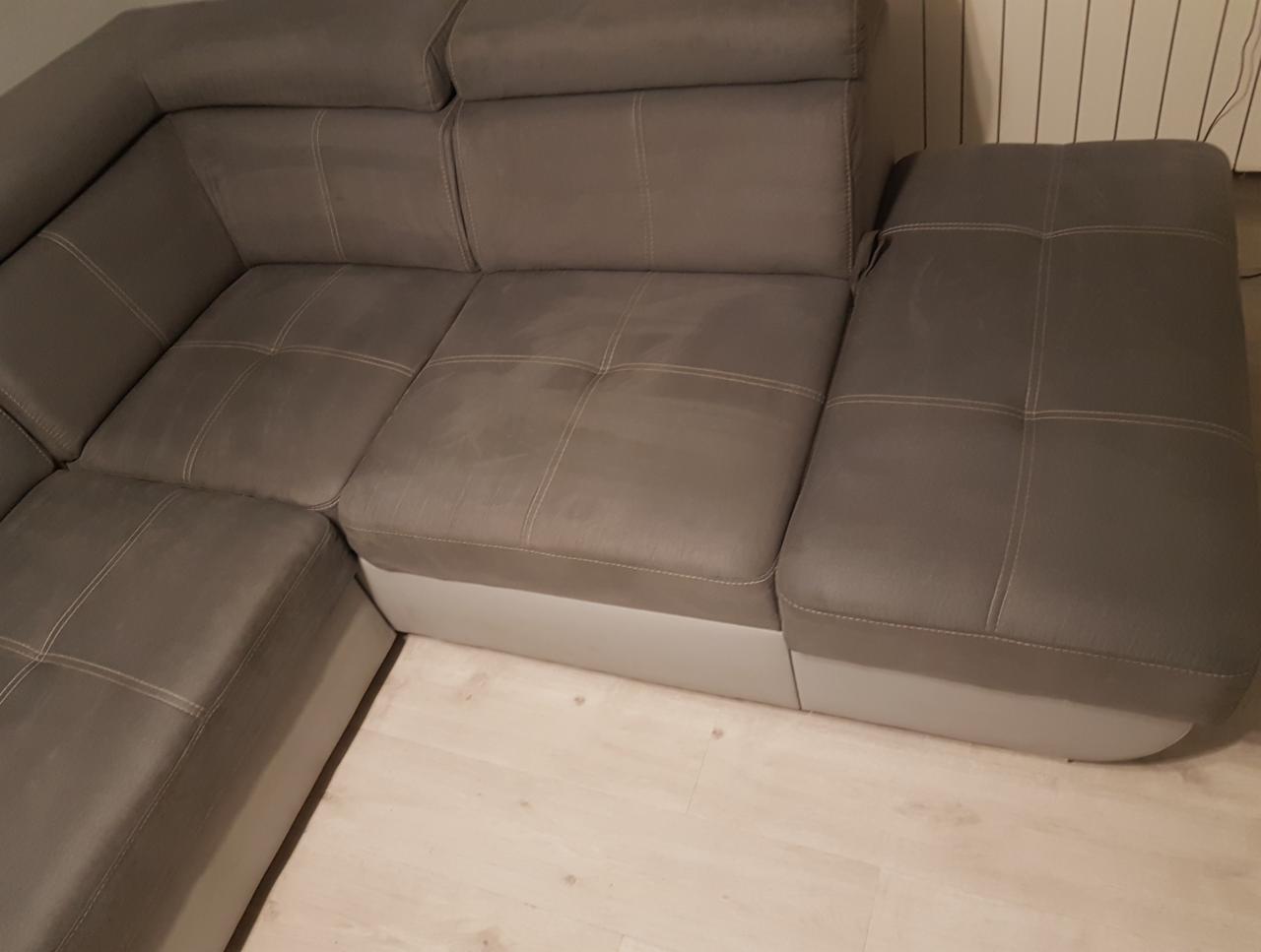 Szary narożnik z widocznymi śladami użytkowania na siedzisku, z białymi przeszyciami i jasną podstawą, ustawiony na podłodze z paneli.