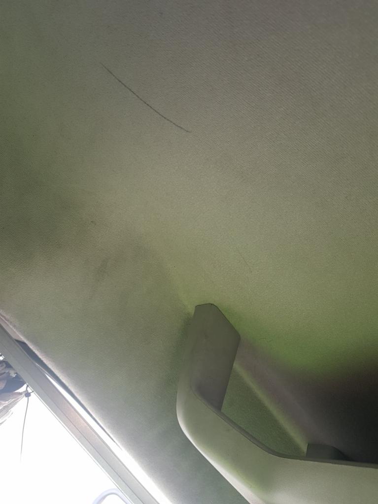 Wnętrze samochodu: Jasna podsufitka z widocznymi zabrudzeniami i zarysowaniami, uchwyt pasażera w kolorze beżowym.