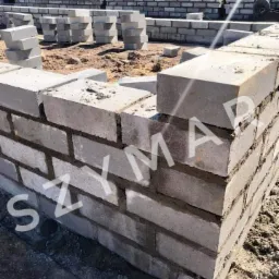 Wznoszenie fundamentów z bloczków betonowych, widoczne spoiny i stosy bloczków w tle.