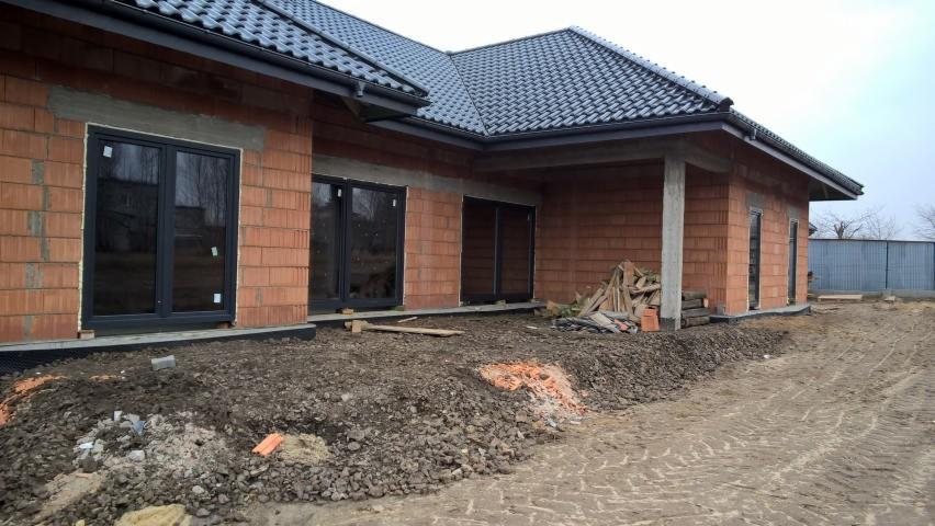 Surowy stan domu z czerwonej cegły z zamontowanymi czarnymi oknami, widoczne przygotowania do dalszych prac wykończeniowych na zewnątrz.