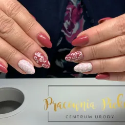 Dłonie z paznokciami żelowymi w odcieniach różu i bieli, zdobione kwiatowymi wzorami; na pierwszym planie logo salonu urody.