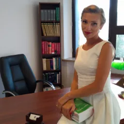 Kobieta w białej sukience siedzi na drewnianym biurku w gabinecie, trzymając książkę o prawie cywilnym; w tle regał z książkami, rzeźba Temidy i lampka z zielonym abażurem.