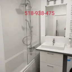 Biała łazienka po remoncie z kabiną prysznicową, umywalką w szafce i grzejnikiem drabinkowym, widoczne płytki na ścianach i pralka z boku.