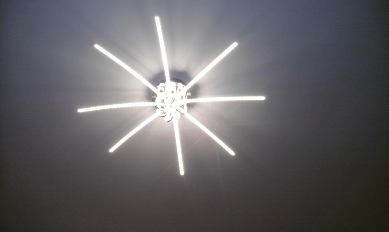 Nowoczesna lampa sufitowa z ośmioma ramionami LED, tworząca wzór przypominający gwiazdę, oświetlająca szary sufit.