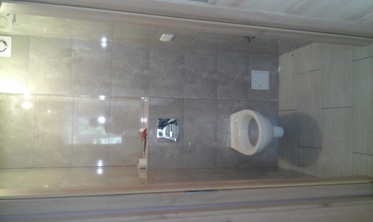 Wykończona łazienka z szarymi płytkami imitującymi marmur na ścianach i podłodze, wisząca toaleta i chromowany przycisk spłuczki.